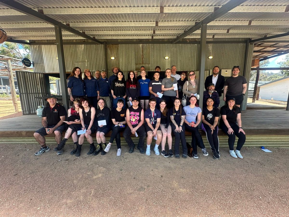 A big group of young people and Raw Potential youth workers smiling together under the Possum Shed at a program day